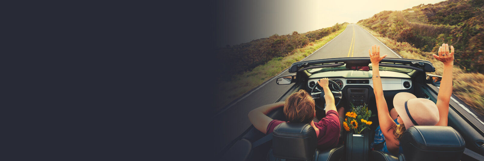 Smiling couple driving in a convertible on an open road at sunset, enjoying a scenic road trip.