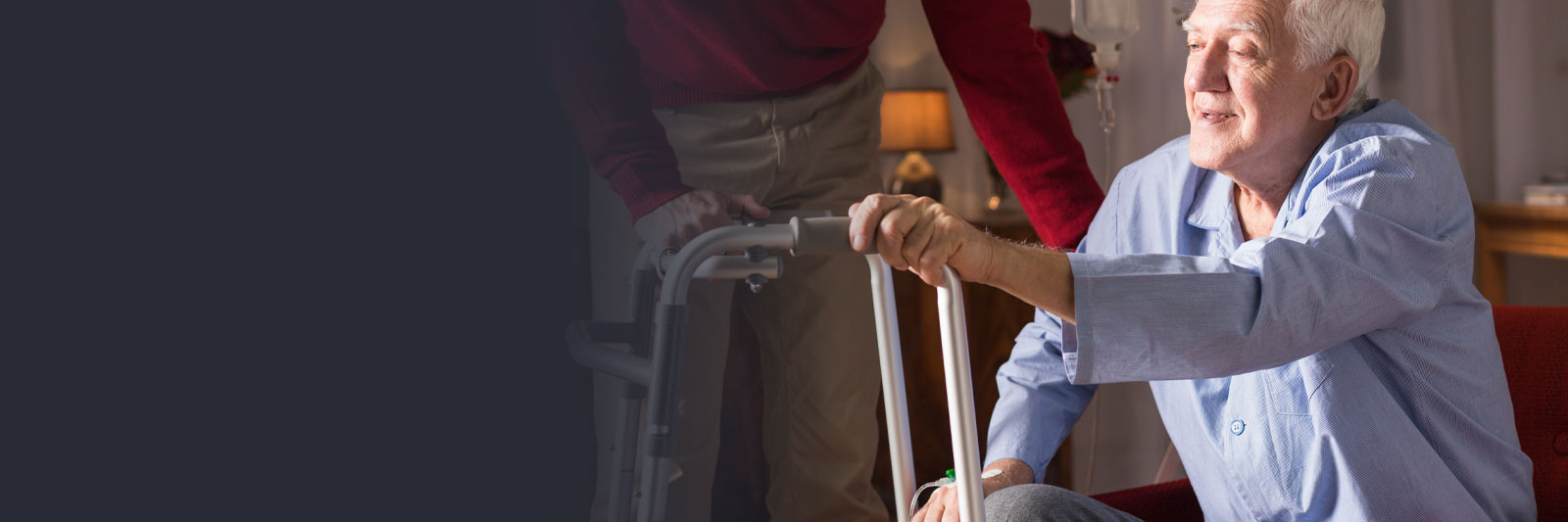 Elderly man smiling while using a walker with assistance in a home or care facility